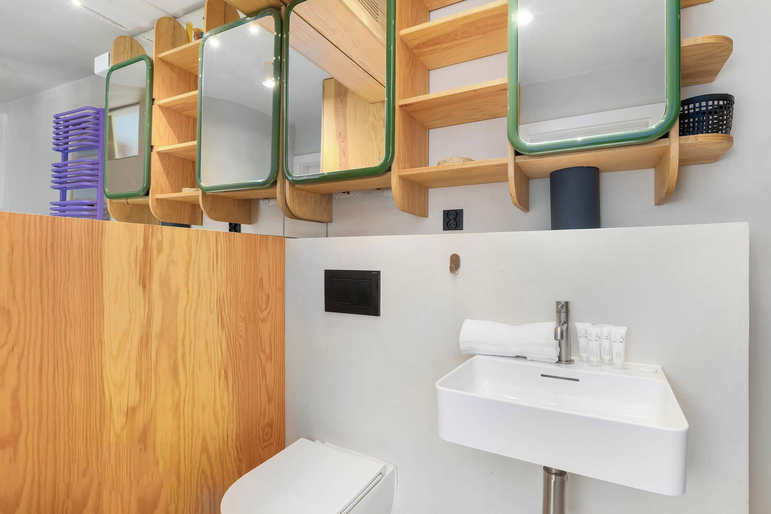 Un baño con un lavamanos blanco, estantes de madera con espejos y un secador de pelo morado.