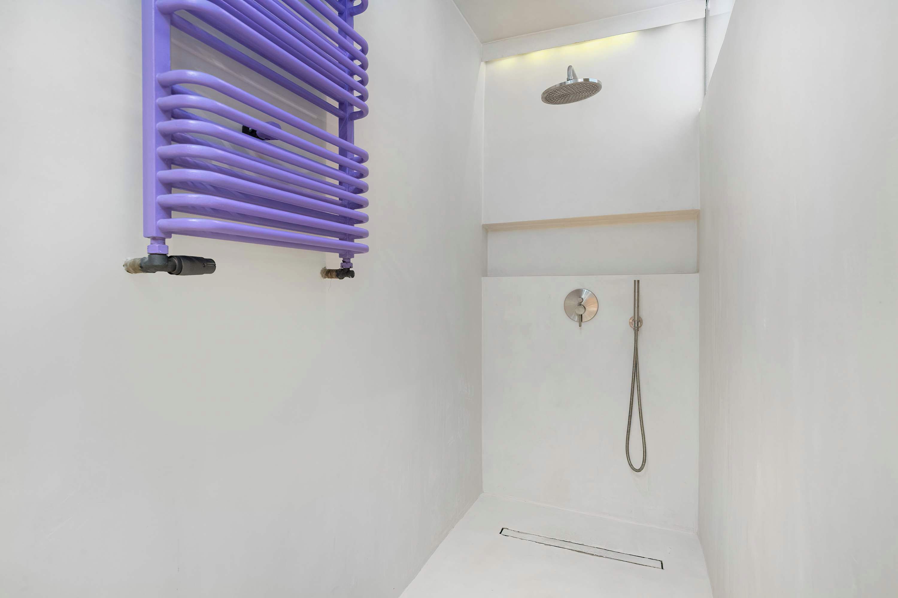 Ein modernes Badezimmer mit einem violetten Handtuchhalter, einer Dusche mit Duschbrausehandstück und einer weißen Wand.