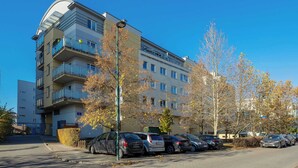 Un edificio residenziale a più piani con balconi, un parcheggio con diverse auto e alberi spogli.