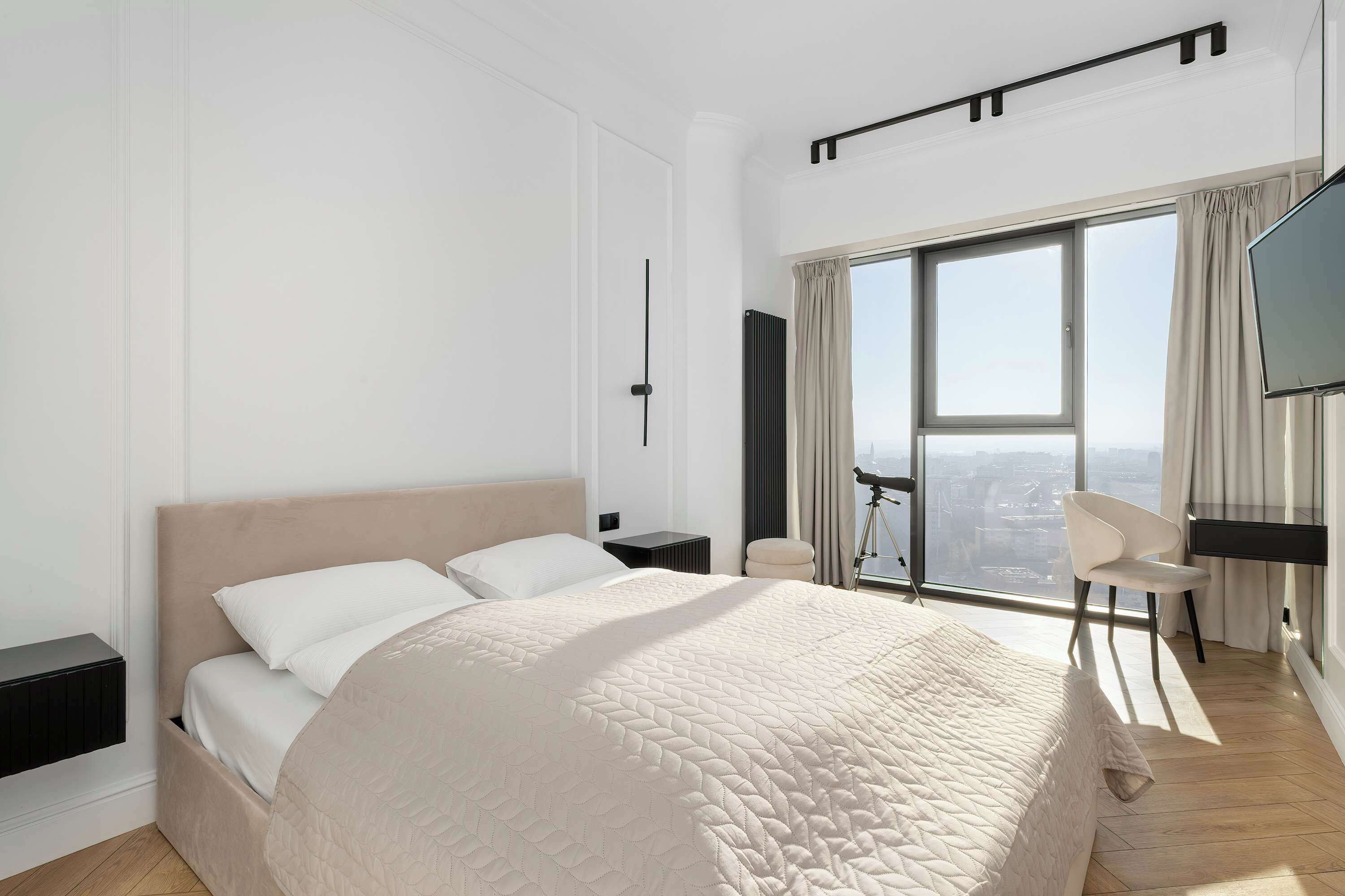 Une chambre d’hôtel moderne dotée d’un grand lit, d’une télévision, d’un fauteuil et d’une grande fenêtre donnant sur la ville.