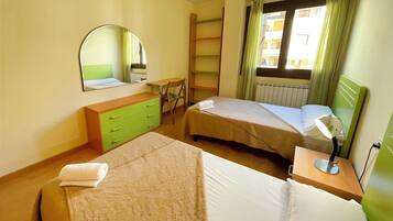 Habitación de hotel con dos camas, un escritorio, una silla, un espejo y un ventanal con cortinas.