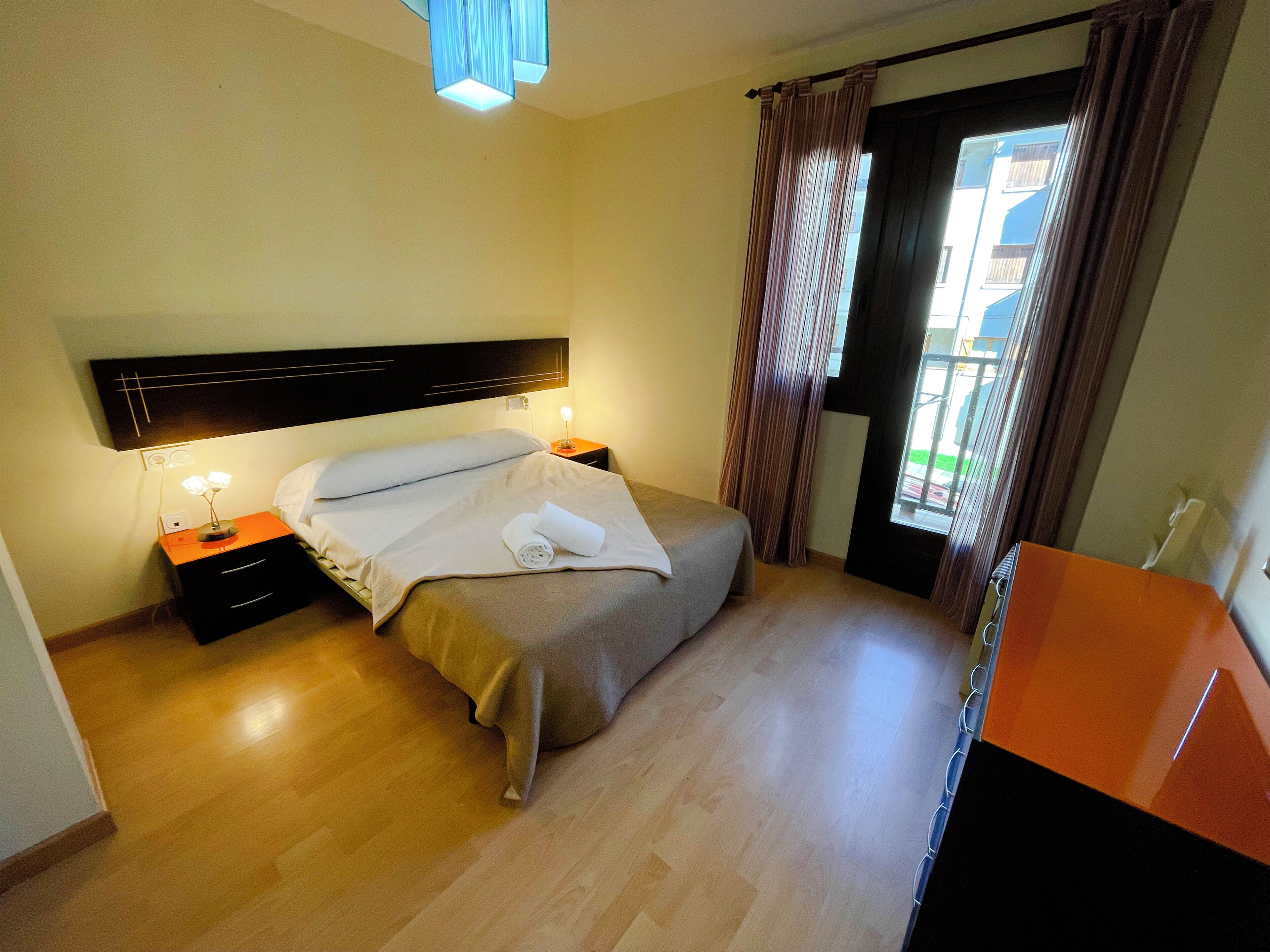 A hotel room with a bed, bedside tables, a desk, and a window with curtains.