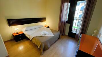 A hotel room with a bed, bedside tables, a desk, and a window with curtains.