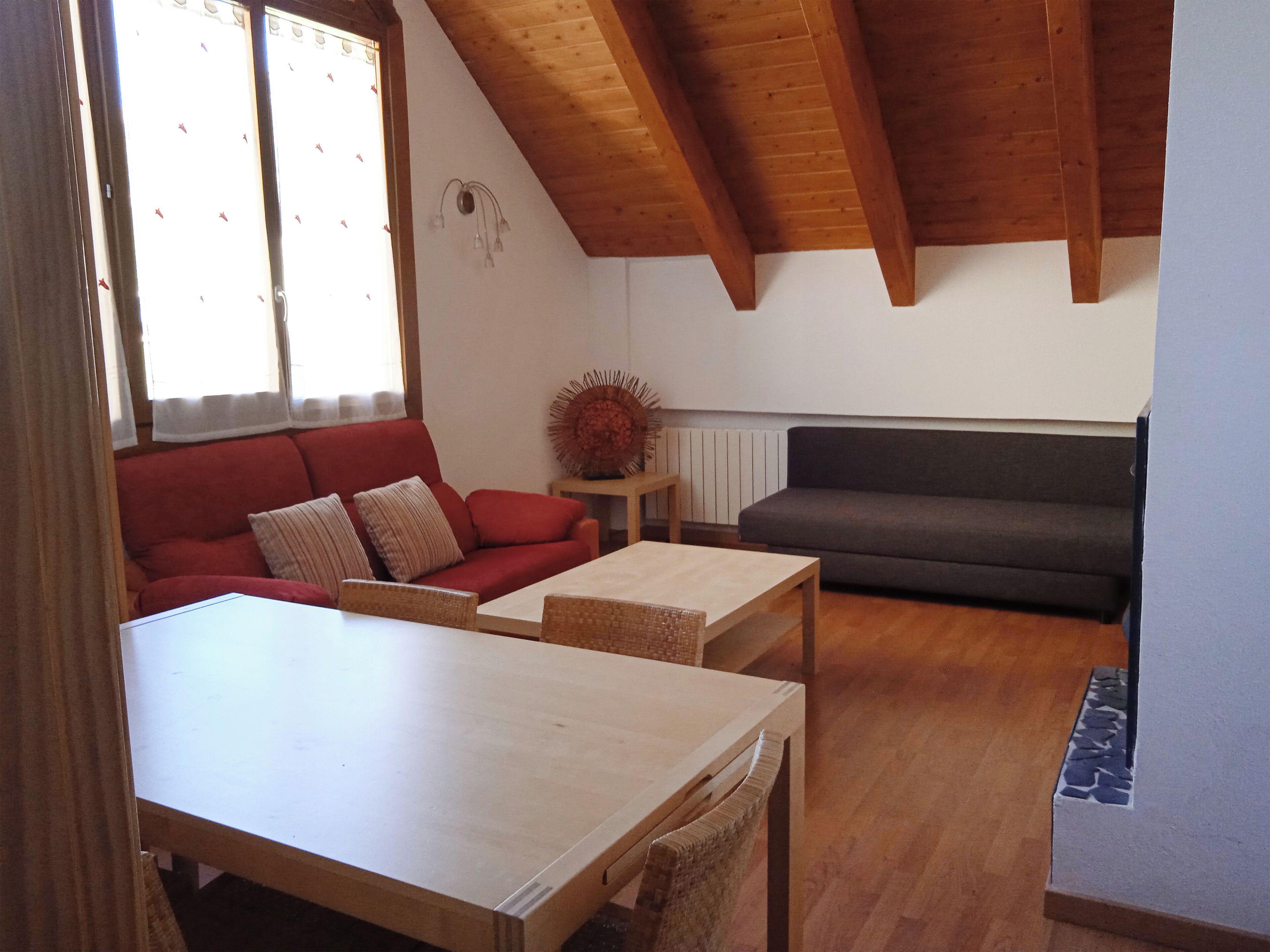 A living room with a red sofa, a grey sofa, a wooden table, and a small side table with a decorative item.