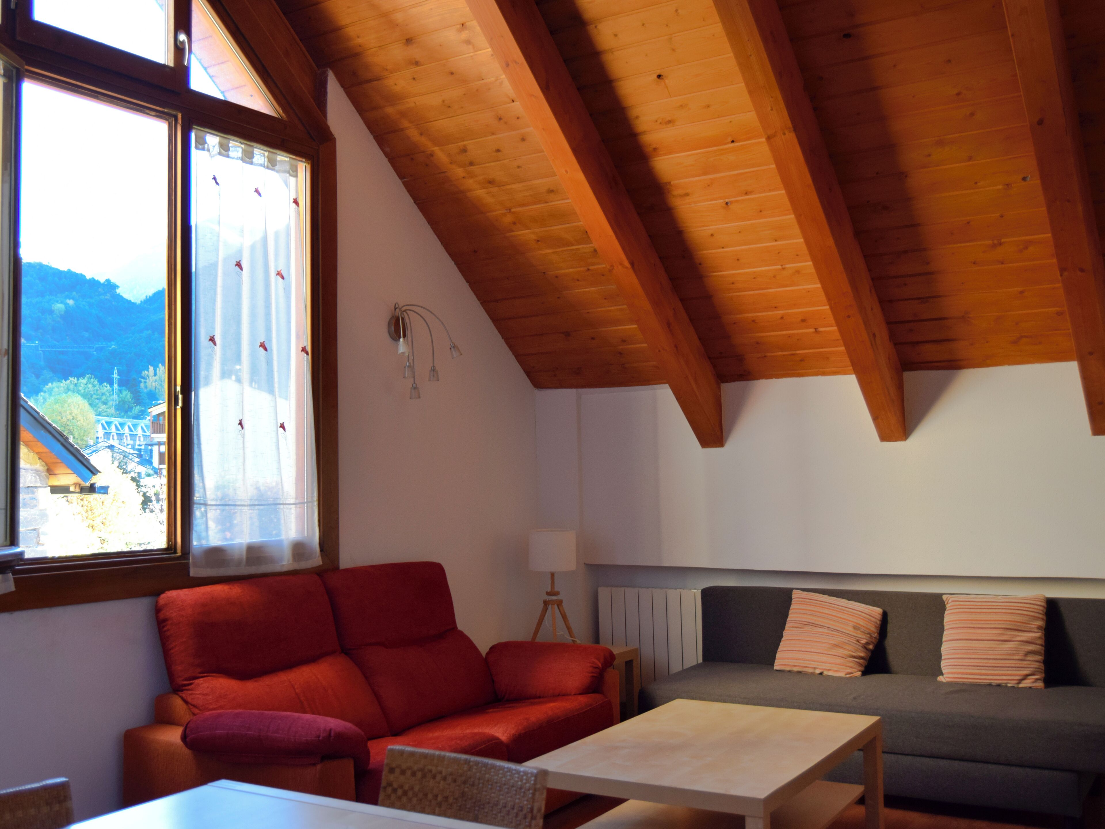 A cozy room with a wooden ceiling, a red sofa, a grey sofa, and a small table.