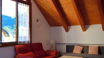 A cozy room with a wooden ceiling, a red sofa, a grey sofa, and a small table.