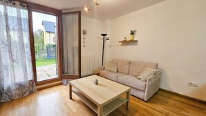 Een woonkamer met een houten vloer, een beige bank met gestreepte kussens, een houten salontafel en een vloerlamp.