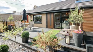 Ein modernes Haus mit einer Terrassenfläche, ausgestattet mit Tisch und Stühlen, umgeben von Kübelpflanzen und einem kleinen Garten.