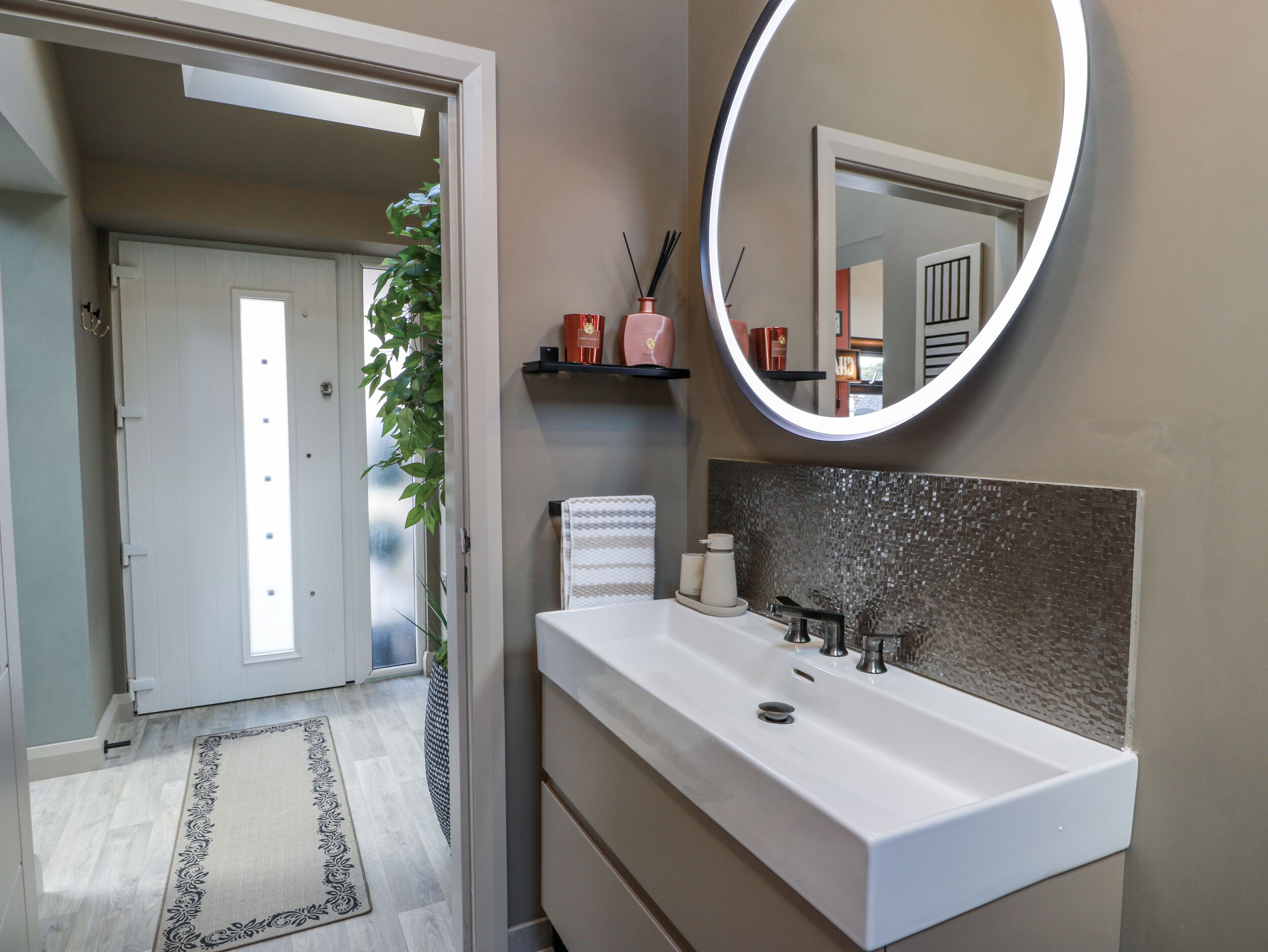 Un baño moderno con un lavamanos blanco, un espejo grande y un estante decorativo con artículos de aseo.