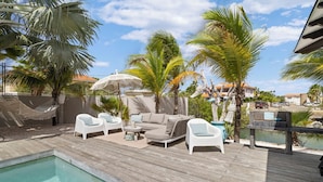 A poolside area with a wooden deck, white lounge chairs, a sofa, and a hammock. - Waterlands Village Bonaire, Kas Palma with private pool! (Kralendijk)