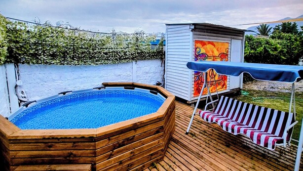 Um deck de madeira com uma banheira de hidromassagem, um pequeno galpão com um mural colorido e vista para um rio.