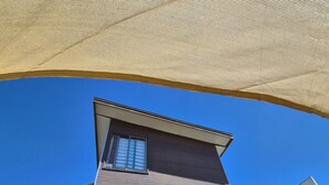 Um edifício moderno com telhado inclinado, janelas grandes e área externa coberta com toldo.