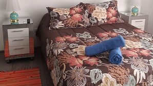 Quarto com cama, mesa de cabeceira, luminária, quadro e tapete.