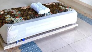 A neatly made bed with a floral-patterned bedspread, a bedside table with a lamp, and a headboard. - Bale Jiwanmukti Narmada (Narmada)