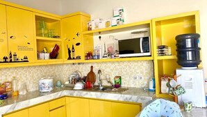 A kitchen with yellow cabinets, a microwave, a water dispenser, and various kitchen items. - Bale Jiwanmukti Narmada (Narmada)