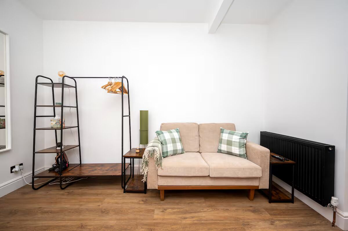 A living room with a beige sofa, a black metal shelf unit, and a radiator.