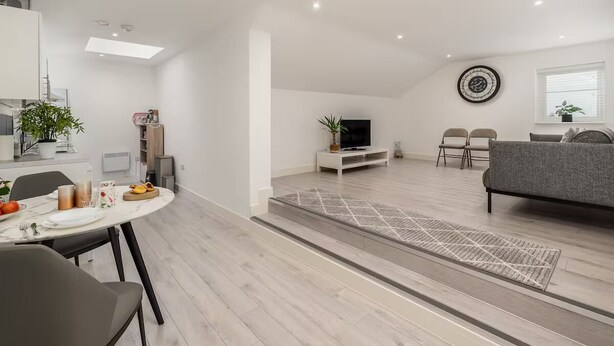 A modern living room with a grey sofa, a TV, and a dining area with a table set for two. - Pass the Keys | Spacious and Quiet Flat in Aylesbury (Aylesbury)