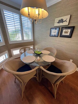 A dining area with a round glass table surrounded by wicker chairs with dark cushions, a chandelier overhead, and a window with blinds. - 3-bedroom townhome in fabulous Longboat Key with stunning views and boat dock (Longboat Key)