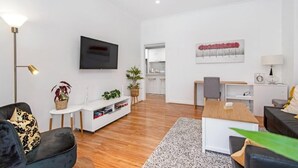 A modern living room with a flat-screen TV, a dining area, and a kitchen in the background. - Ruthven Mansions CBD Boutique NY-Style Apartment (Adelaide)