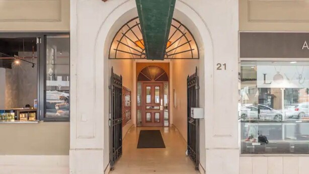 An entrance with a glass door, a black mat, and a number '21' on the wall. - Ruthven Mansions CBD Boutique NY-Style Apartment (Adelaide)