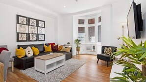 A modern living room with a black sofa, a white coffee table, and a black armchair. There are framed artworks on the wall and a large window with a view. - Ruthven Mansions CBD Boutique NY-Style Apartment (Adelaide)