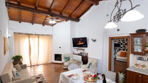 Ein Wohnzimmer mit Kamin, einem gedeckten Esstisch, einem Fernseher und einer Küche mit Steinwand.