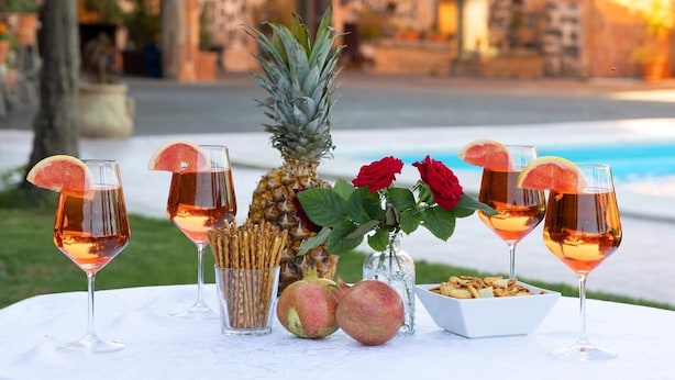 Ein Tisch mit Getränken, Früchten und einer Schale Snacks, draußen mit Pool und Gebäuden im Hintergrund.