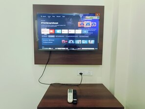 Een flatscreen televisie bevestigd aan een muur boven een houten tafel met een afstandsbediening erop.
