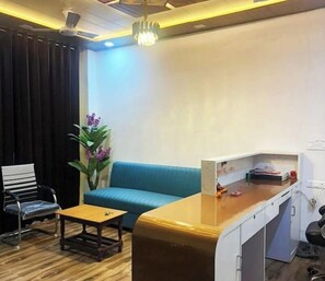 Een kamer met een blauwe bank, een houten tafel, een stoel, een bureau met een computer en een plant.