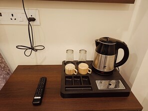 Una cafetera con dos tazas y un control remoto sobre una mesa de madera.