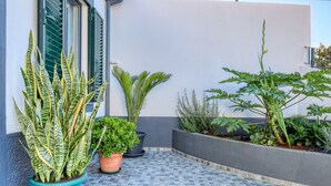 Une terrasse carrelée agrémentée de plantes en pot et un bâtiment doté de volets.