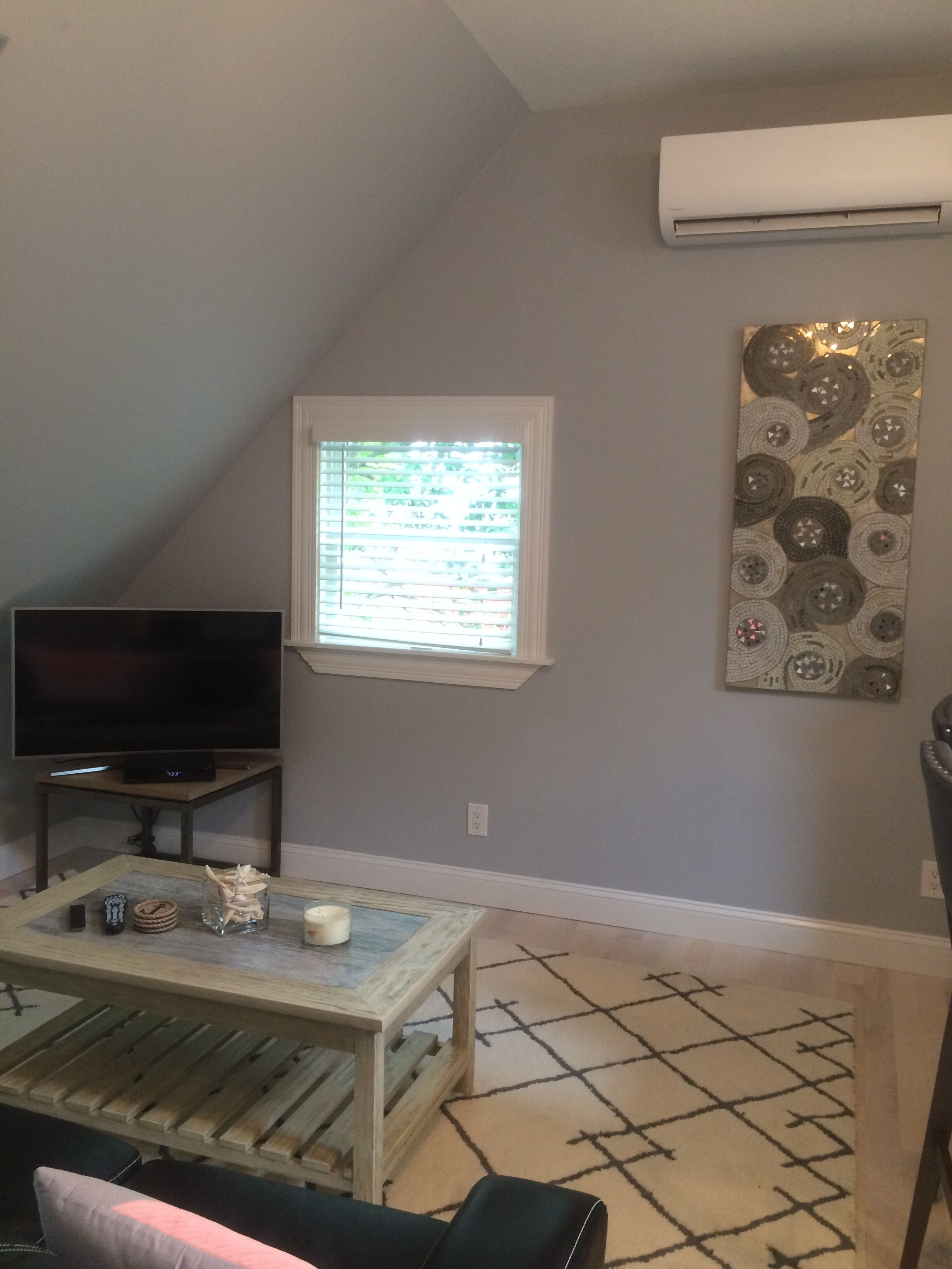 A living room with a television, a window, a patterned wall art, and a patterned rug.