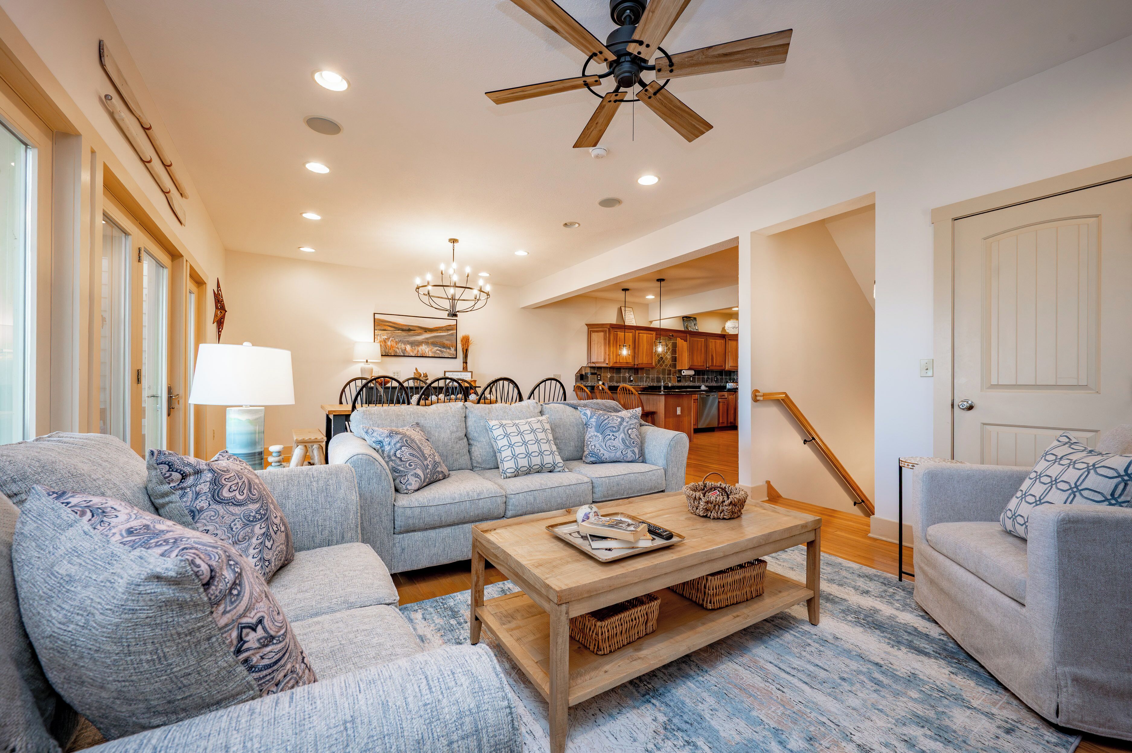 A spacious living room with a grey sofa set, a wooden coffee table, and a ceiling fan.