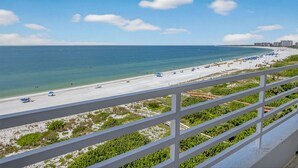 Blick auf einen Strand vom Balkon mit Geländer, klarer Himmel und ruhiges Meer.