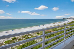 Blick auf einen Strand vom Balkon mit Geländer, klarer Himmel und ruhiges Meer.