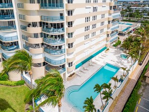Ein mehrstöckiges Hotel mit Balkonen, einem Swimmingpool und Palmen.