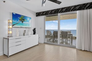 Ein modernes Wohnzimmer mit einem großen Flachbildfernseher, einem weißen Schrank und einem Balkon mit Gartenmöbeln.