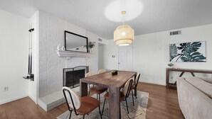 Een eetruimte met een houten tafel, stoelen, een hanglamp en een open haard.
