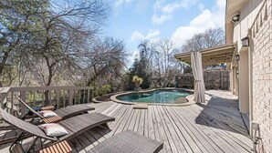 Een houten terras met een hottub, lounge fauteuils en een pergola.