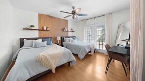 Een moderne slaapkamer met twee bedden, een plafondventilator, een wand van houten panelen en een zithoek met een tafel en stoelen.