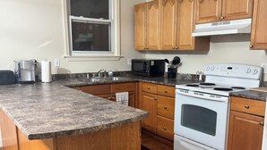 A modern kitchen with granite countertops, wooden cabinets, a stainless steel trash can, and a built-in oven. - Downtown Detroit Getaway (Detroit)