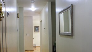 A hallway with wooden flooring, a black rug, a door with a silver handle, and a framed mirror on the wall. - Downtown Detroit Getaway (Detroit)