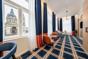 Habitación de hotel con un ventanal grande, alfombra a cuadros y vistas a un edificio histórico.