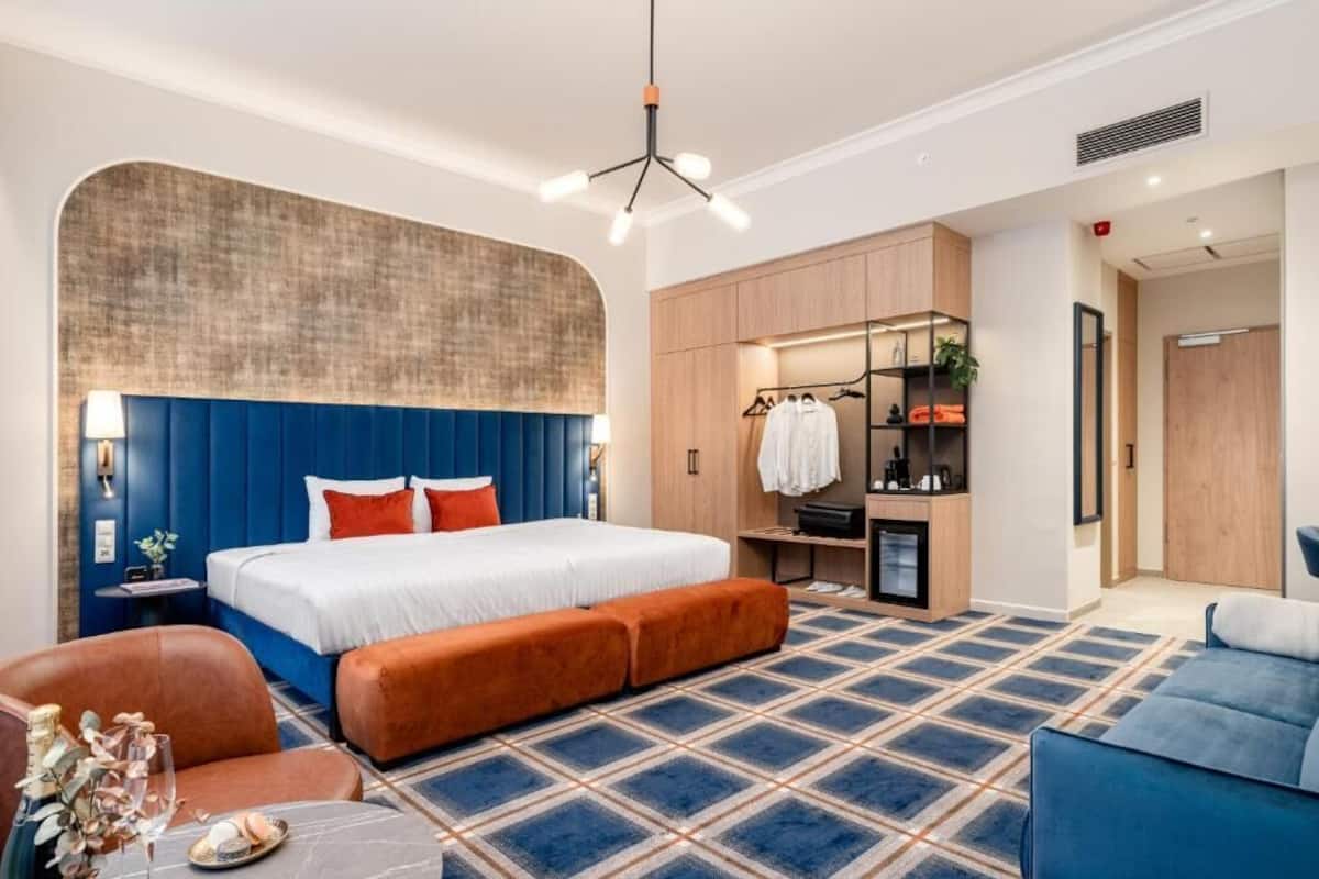 Una habitación de hotel moderna con una cama grande, una zona de estar con sofá y sillón, un escritorio pequeño y un armario.
