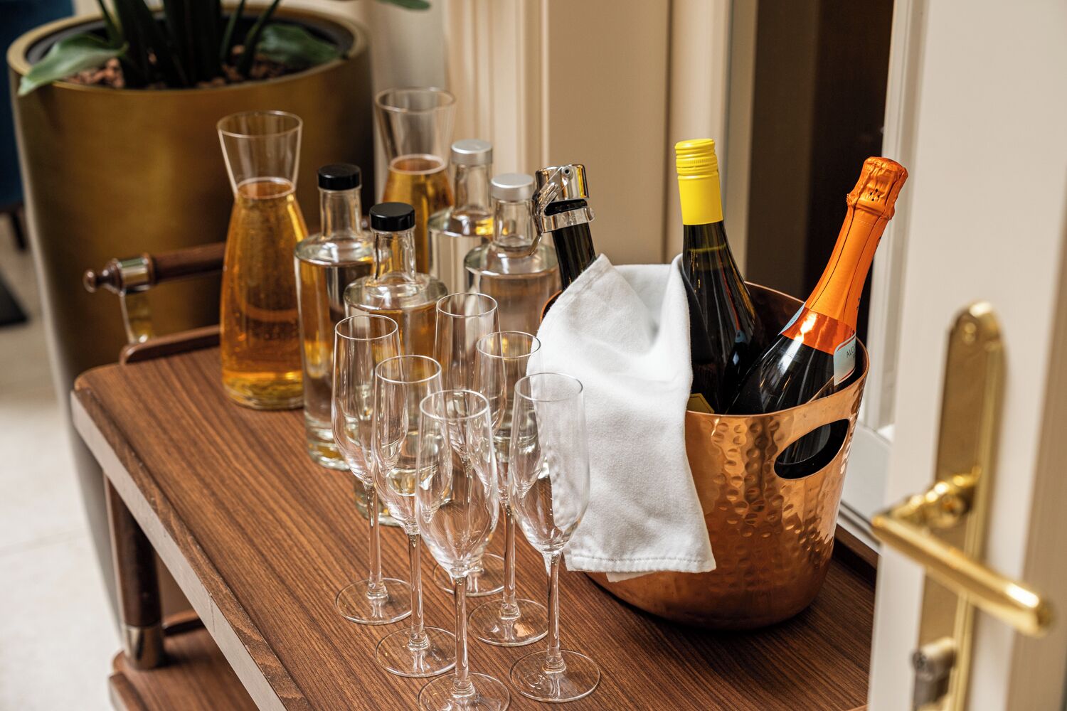 A wooden bar cart with wine bottles and glasses.