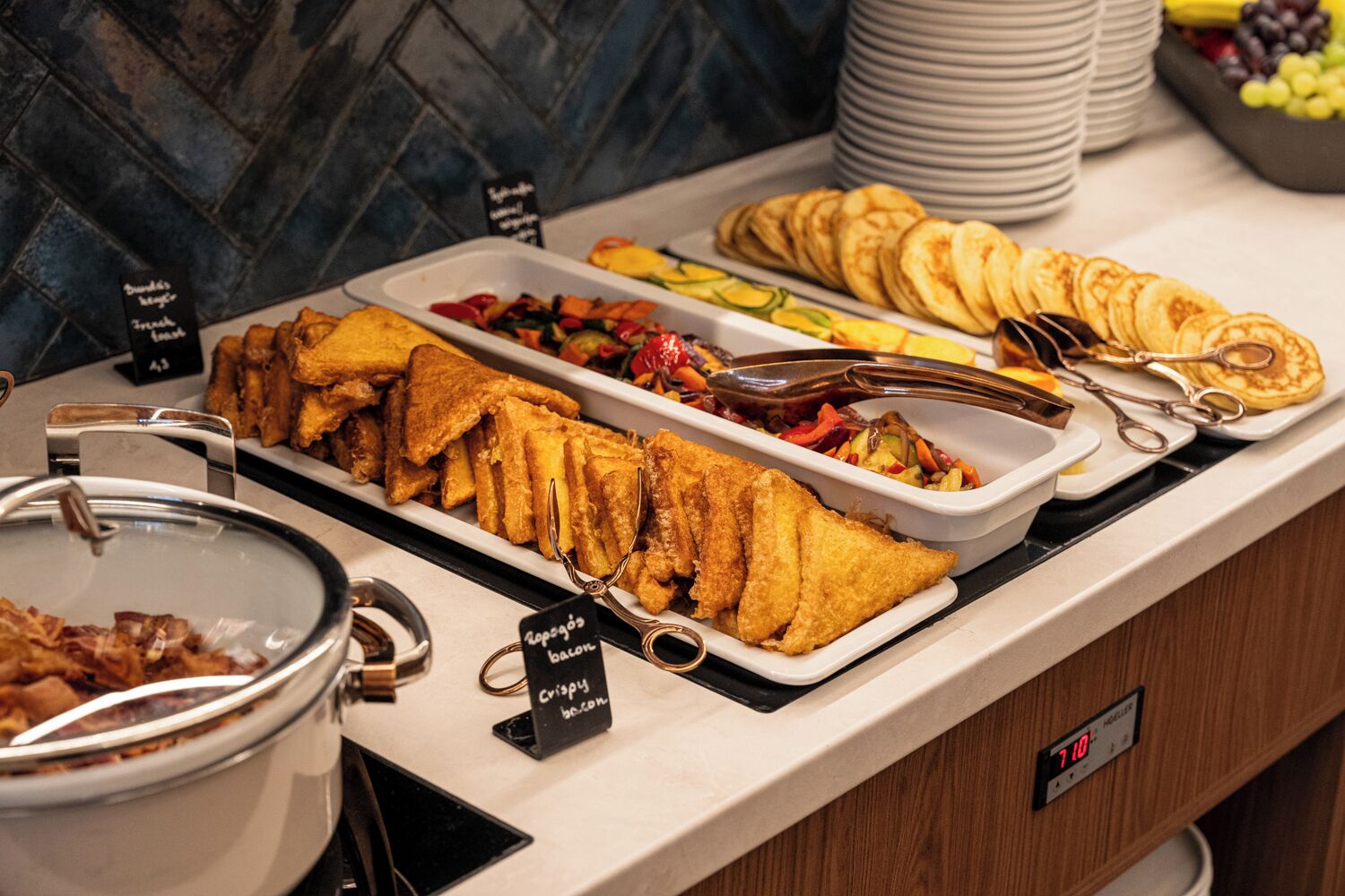 A buffet with various food items including fried fish, bacon, and pancakes.