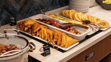 A buffet with various food items including fried fish, bacon, and pancakes.