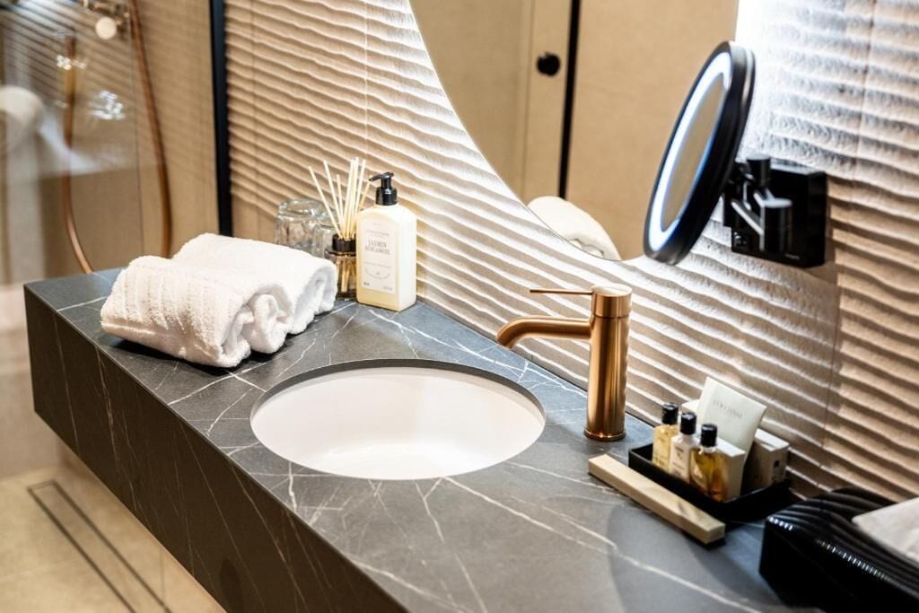 A modern bathroom with a marble sink, a towel, a soap dispenser, and a mirror.