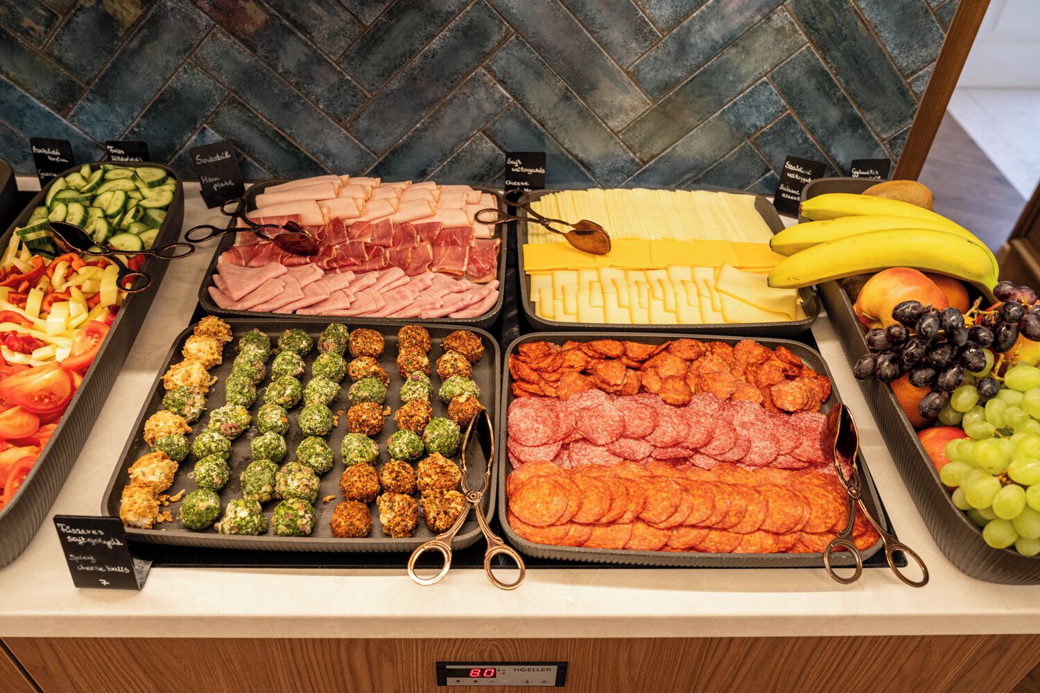 A buffet with various food items including meats, cheeses, fruits, and vegetables.
