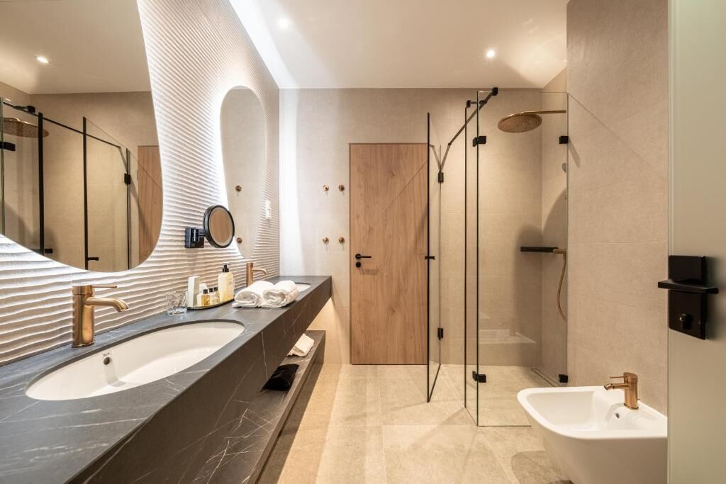 Un baño moderno con un espejo grande, dos lavamanos, una ducha y una puerta de madera.